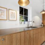 Küche mit Holzschränken, Edelstahl-Arbeitsplatte und Fenster.