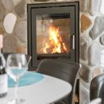 Feuer im Kamin, Tisch mit Weinglas und Flasche, schwarze Sessel