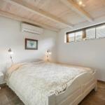 Schlafzimmer mit Bett, Nachttisch und Fenster. Holzdecke und Klimaanlage.