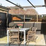 Terrasse mit Tisch, Stühlen und Blumen. Hintergrund: Holzzaun und Wald.