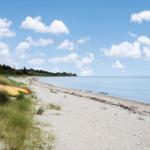 Beach with sand, grass, and a yellow kayak under a blue sky with white clouds.
