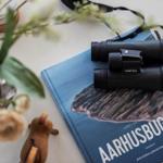 A book with binoculars on top and flowers beside it.