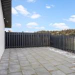 Terrace with stone slabs and black wooden border. Background: forest and blue sky.
