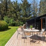 Deck with table and chairs beside a black wooden house. Background: green lawn and trees.
