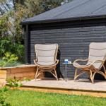 Two rattan chairs with cushions are on a terrace in front of a house.