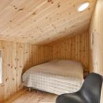 Bedroom with wooden walls, bed, and chair. Window with view of greenery.