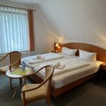 Room with double bed, two nightstands, chair and table. Window with curtains.