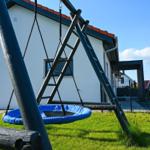 Ein blauer Klettergerüst mit Schaukel steht im Garten vor einem Haus.