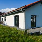 Moderne Villa mit Terrasse und Garten. Rotes Dach und weiße Fassade.