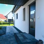 Moderne Eingangstreppe mit schwarzem Holz und grauem Kiesweg führt zur Haustür.