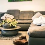 Ein grauer Sofa-Bereich mit Kissen, Decke und einem runden Tisch mit Blumen.