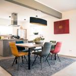 Essbereich mit Tisch und bunten Stühlen. Küche mit Arbeitsplatte und Fenster.