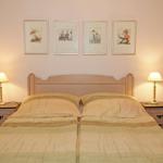 Doppelbett mit zwei Nachttischen und Lampen. An der Wand hängen vier gerahmte Bilder.