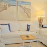 Wohnzimmer mit Sofa, Sessel und Tisch. Wandbilder zeigen Strand. Stehlampe mit Holzgestell.
