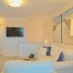 Wohnzimmer mit Sofa, Fernseher und Strandmotiv an der Wand.