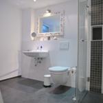 Badezimmer mit Dusche, Waschbecken und Toilette. Fliesen und Spiegel sind sichtbar.