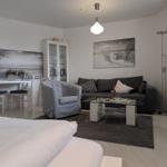 Wohnzimmer mit Sofa, Sessel und Esstisch. Wandbild zeigt Strand.