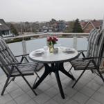 Terrasse mit Tisch und zwei Stühlen, gedeckt für zwei Personen mit Blumen und Gläsern.