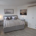 Schlafzimmer mit Bett, Kleiderschrank und Wandbildern.