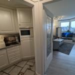 Küche mit weißen Schränken und Mikrowelle. Wohnzimmer mit Fernseher und Fenster.