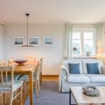 Wohn- und Essbereich mit Sofa, Tisch und Stühlen sowie Fenster mit Vorhängen.