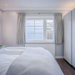 Schlafzimmer mit Bett, Nachttisch und Fenster mit Vorhängen.