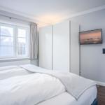 Schlafzimmer mit Bett, Kleiderschrank und Fernseher an der Wand.