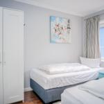 Zimmer mit zwei Betten, Kleiderschrank und Fenster mit Vorhängen.