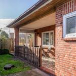 Rotes Backsteinhaus mit Terrasse und Garten. Holzgeländer und Sitzgelegenheit.