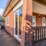 Rotes Backsteingebäude mit Holzterrasse und Gartentür. Holzgeländer und Fenster sind sichtbar.