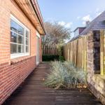 Holzterrasse neben Backsteinhaus mit Steinmauer und Holzzaun.