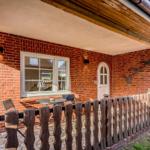 Terrasse mit Tisch, Stühlen und Holzzaun vor rotem Backsteinhaus mit Fenster und Tür.