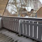 Balkon mit Holzgeländer und Schnee, Blick auf verschneite Häuser und Bäume.