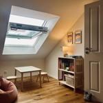 Dachgeschosszimmer mit Tisch, Stühlen, Bücherregal und Dachfenster.
