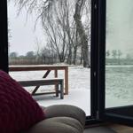 Durch große Fenster blickt man auf eine schneebedeckte Terrasse mit Holztisch und Bank.