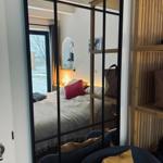 Schlafzimmer mit Bett, Spiegel und Holzregal. Fenster zeigt Außenbereich.