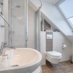 Badezimmer mit Dusche, Waschbecken und WC unter Dachschrägen mit Fenster