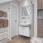 Badezimmer mit Dusche, Waschbecken und Heizkörper für Handtücher.