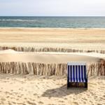Ein blaues Strandkörbchen steht auf sandigen Dünen vor dem Meer.