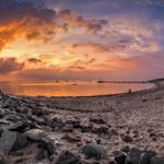 Strand bei Sonnenuntergang mit Steinschutz und Strandkörben.