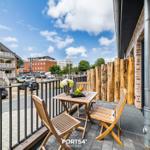 Terrasse mit Holztisch, Stühlen und Obstschale. Blick auf Straße und Gebäude.