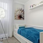 Schlafzimmer mit weißem Bett, blauer Decke und Wandbild. Neben einem Fenster steht eine Stehlampe.