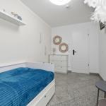 Schlafzimmer mit weißem Bett, blauer Bettdecke, Schrank und Wanddekoration.