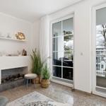 Wohnzimmer mit Kamin, Pflanzen und Terrassentür. Blick auf Balkon mit Garten.