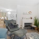 Wohnzimmer mit Sessel, Kamin und Küchenbereich im Hintergrund.