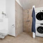 Badezimmer mit Dusche, Toilette und Waschmaschine-Trockner-Kombination.