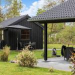 Schwarze Holzhütte mit Terrasse und Gartenmöbeln unter einem Dach.
