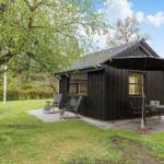 Schwarze Holzhütte mit Terrasse, Sitzgelegenheiten und Sonnenschutz im Grünen.