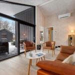 Wohnzimmer mit braunen Ledermöbeln, Holzwand und großem Fenster zur Terrasse.