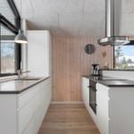 Moderne Küche mit weißen Schränken, Holzwand und großem Fenster. Edelstahl-Abluft und Kaffeemaschine.